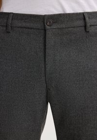 Graue, strukturierte Hose mit flacher Vorderseite, horizontalem Stoffmuster und einem einzelnen Knopfverschluss an der Taille.
