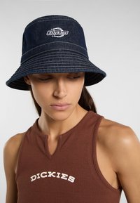 Cappello a secchi in denim blu marino con logo "Dickies" bianco. Visiera ampia e morbida; dettagli di cucitura sottili; tessuto texturizzato; design casual.