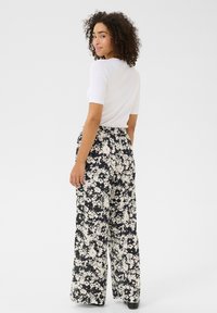 Pantalons larges floraux noir et blanc avec une taille élastique. Le mannequin porte un haut ajusté blanc, offrant une silhouette décontractée.
