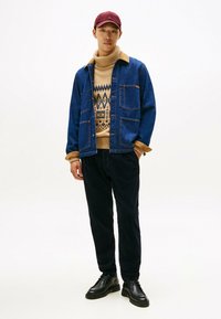 Denimtakki, jossa on bége corduroy-kaulus, kuvioitu bége neulepaita, tummat housut ja mustat kengät, päällä marooni hattu.