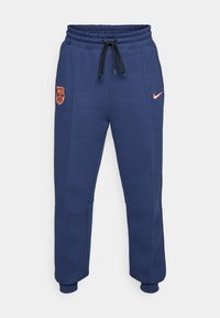Pantalons de survêtement bleu marine en matériau doux, avec une taille élastique à cordon de serrage, des poches latérales et un logo Nike orange avec un emblème de Barcelone.