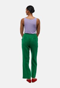 Débardeur violet, pantalon ample vert avec taille élastique et poches arrière, associé à des chaussures rouge à enfiler, vu de dos.