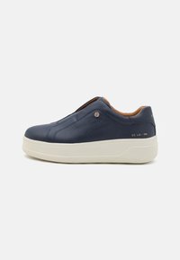 Marineblå slip-on sko med teksturert læroverdel, lys gummisåle og gullfarget merke på hælen.