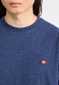 Tricou bleumarin cu print, cu guler rotund. Prezintă un mic logo brodat colorat pe piept. Textură moale, casual.