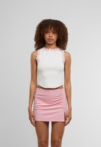 Haut court sans manches blanc avec une bordure festonnée rose ; associé à une mini-jupe rose ajustée avec une fente sur le côté et un détail froncé.