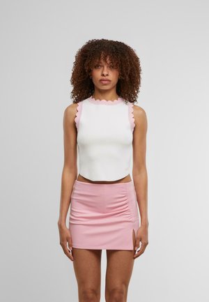 Hvid ærmeløs crop top med en bølget lyserød kant; parret med en tætsiddende lyserød miniskirt med en sidenedskæring og rynkede detaljer.