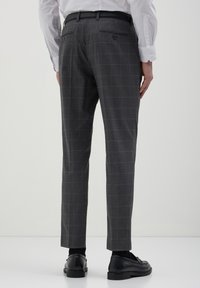Grau karierte Hosen mit schlanker Passform, glatter Textur und zwei Gesäßtaschen mit Knopfverschlüssen. Tragen mit einem schwarzen Gürtel und Schuhen.
