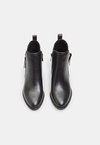 Botas de cuero negras hasta el tobillo con punta afilada, detalles de cremallera en los laterales y tiradores en la parte trasera para ponérselas fácilmente. Textura suave.