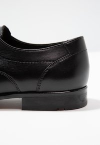 Schwarzer Lederschuh mit glatter, glänzender Oberfläche, runder Zehenform, dezenten Nähdetails und einem niedrigen, soliden schwarzen Absatz.