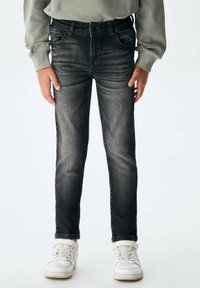 Vaqueros de denim negro con un corte ajustado, un ligero desvanecimiento, cinco bolsillos y pasadores para cinturón, combinados con zapatillas blancas.