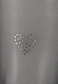 Tissu gris métallique présentant une forme de cœur faite de petits clous argentés, sur un fond en maille texturée.
