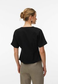 Mustast lühikeste varrukatega ülaosa, mis on valmistatud siledast kangast ja millel on lõdvestunud istuvus ning peen õmbluse detail. Kombineeritud helehallide ülikonnapükstega.