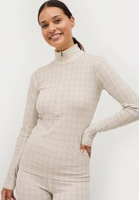 Lange mouwen, hoge hals top in lichtbeige met een gestructureerd geometrisch patroon, voorzien van een rits bij de kraag en aansluitende mouwen.