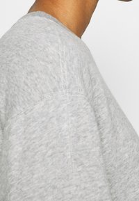 Harmaa puuvillainen T-paita, jossa on pyöreä pääntie, lyhyet hihat ja näkyvät ompelusaumat. Kangas näyttää pehmeältä ja siinä on rento rakenne.