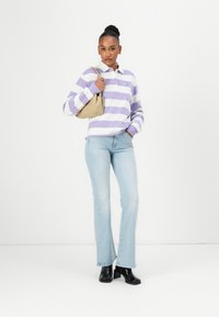 Striped purple and white long-sleeve polo, light blue flared jeans, black heeled boots, carrying a beige handbag. Simple design; casual fit.