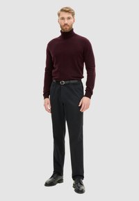 Bordeaux coltrui, op maat gemaakte zwarte broek en zwarte schoenen. De trui heeft lange mouwen en een getailleerde pasvorm.
