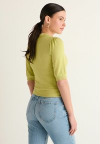 Grøn strikket sweater med korte pufærmer og ribbet kant, parret med lyseblå denimjeans med baglommer og falmet tekstur.