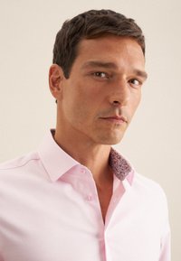 Lichtroze overhemdd met een patroon van donkere bloemen aan de binnenkraag, knoopsluiting aan de voorkant, een getailleerde pasvorm en een soepele textuur.