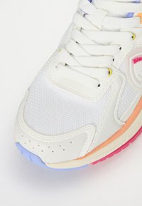 Baskets blanches avec une tige en mesh, accents multicolores en orange, rose et bleu, semelle texturée et système de laçage prononcé.