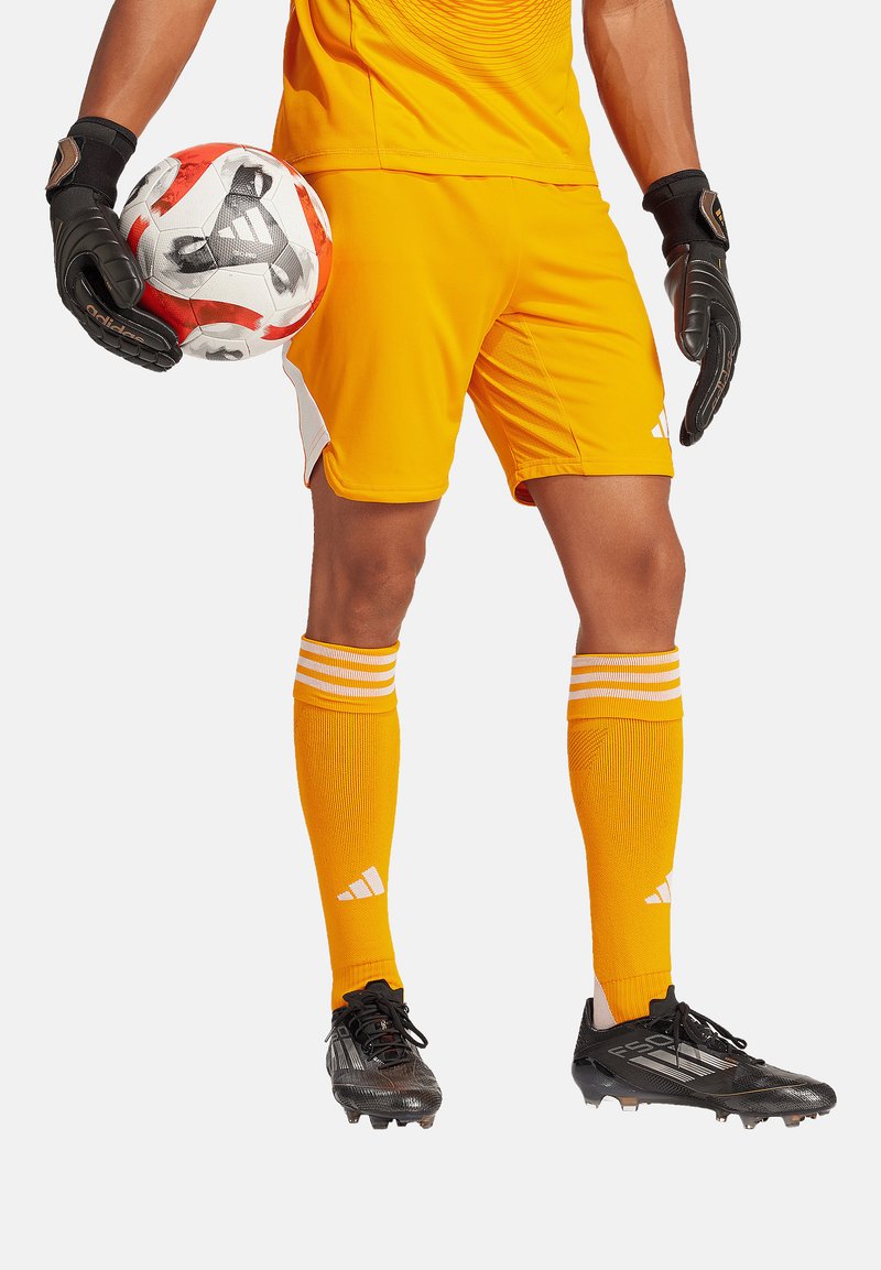Oranje soccer doelmanuitrusting met zwarte handschoenen, gestreepte oranje sokken en zwarte voetbalschoenen. Bevat een patroon op het shirt en een kleurrijke bal.