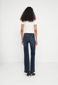 Blugi evazați de culoare albastru închis, confecționați din material denim, cu talie medie, cinci buzunare și un design clasic cu o textură ușor decolorată.