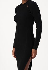 Abito nero a maglia a coste con maniche lunghe, spacco laterale e dettaglio cut-out sulle spalle, caratterizzato da un silhouette aderente.