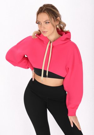 Fényes rózsaszín, cropped kapucnis pulcsi húzózsinórral, ejtett vállakkal és sima textúrával, fekete leggings-szel párosítva.