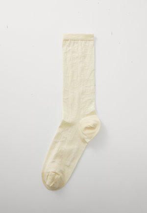 Knee-high socks in pale yellow cotton blend, featuring a subtle floral texture and reinforced toes. Smooth finish with a ribbed cuff.