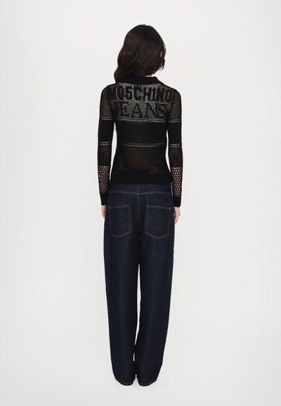 Melnas, adītas acs ilgas piedurknes krekliņš ar uzrakstu "MOSCHINO JEANS", apvienots ar platām kājām tumšā džinsa biksēm, kurām ir klasiskā piecu kabatu dizains.