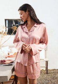 Set de pijama din mătase în roz pal, cu un top cu nasturi și guler, decorat cu modele în formă de inimă, pantaloni scurți lejeri cu manșete contrastante, textură netedă.