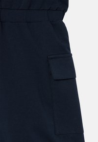 Μπλε στρατιωτικού τόνου βαμβακερή φόρμα με ελαστική μέση και πλευρική τσέπη με καπάκι. Το ύφασμα έχει ομαλή, ελαφρώς υφασμάτινη φινίρισμα.