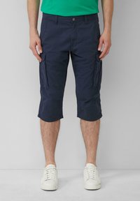 Shorts cargo en tissu léger de couleur marine, avec poches avant et latérales, et d'une longueur jusqu'aux genoux. Associés à des baskets blanches.