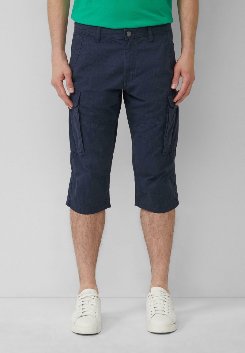 Shorts cargo en tissu léger de couleur marine, avec poches avant et latérales, et d'une longueur jusqu'aux genoux. Associés à des baskets blanches.
