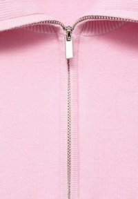 Sweatshirt zippé rose clair avec une fermeture éclair argentée, col côtelé et texture douce, présentant un design sans couture à l'avant.