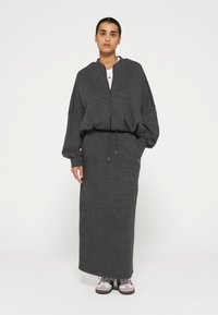 Dunkelgrauer Reißverschluss-Pullover mit weiten Ärmeln, kombiniert mit einem passenden langen Rock. Beide Teile haben eine weiche Textur und minimale Details.