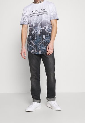 Weißes T-Shirt mit schwarzem Aufdruck "OUTLAW", das ein Gradient-Design mit Ketten und floralen Mustern aufweist. Kombiniert mit dunklen Jeans und weißen Schuhen.