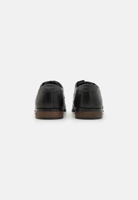 Pantofi din piele neagră cu finisaj neted, vârful rotund și toc mic. Prezintă o talpă din lemn și un design minimalist.