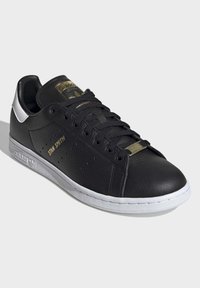 Schwarze Leder-Sneaker mit weißer Sohle und Akzenten. Verfügt über goldene Branding-Elemente auf der Zunge und der Seite, eine strukturierte Oberfläche und eine Schnürung.