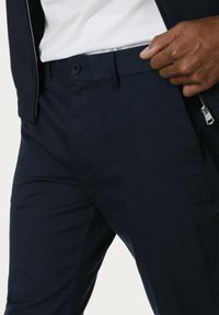 Pantalones azul marino con una textura suave, cierre de botón en la cintura y un bolsillo con cremallera en el lateral.