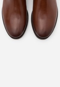 Bottines en cuir marron avec une finition lisse, un bout arrondi et une semelle noire contrastante avec des détails de couture.