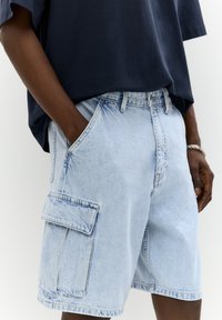 Svetlo modri jeans kratki hlače z sproščenim krojem, sprednjimi in stranskimi žepi ter velikim cargo žepom na levi nogi. Mehka tekstura tkanine.