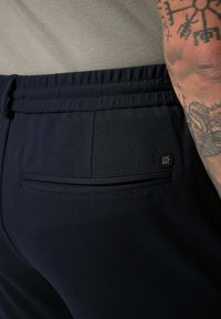 Marinefarbene Sporthosen mit elastischem Bund, ausgestattet mit einer Gesäßtasche und subtilen Logo-Details. Der Stoff hat eine glatte Textur.