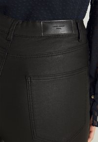 Black faux leather high-waisted jeans featuring a smooth texture, back pockets, and a brand label on the waistband.