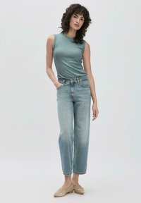 Top sans manches bleu clair avec un col rond, associé à un jean décontracté en denim clair. Des chaussures plates beiges et les mains glissées dans les poches complètent le look.