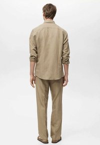 Lysebrune, stribede skjorte og matchende bukser. Stoffet ser blødt ud med en afslappet pasform. Bagsiden viser opkrøllede ærmer og afslappede sandaler.