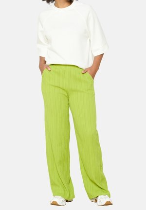 White ribbed sweatshirt with oversized sleeves paired with green, textured, wide-leg pants featuring an elastic waistband.