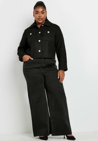 Svart cropped jacka med texturerad väv och guldknappar, kombinerad med högmidjade vida svarta jeans. Slät yta och skräddarsydd passform.