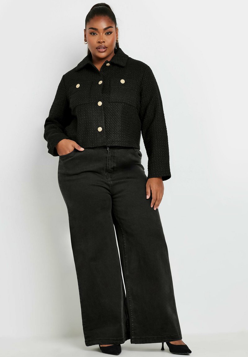 Svart cropped jacka med texturerad väv och guldknappar, kombinerad med högmidjade vida svarta jeans. Slät yta och skräddarsydd passform.