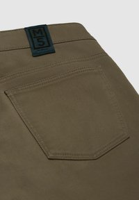 Khaki broek met een textuurstof, een achterzak met dubbele stiksels en een blauw merklabel op de tailleband.