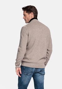 Beige gebreide trui met een zwarte kraag, voorzien van een gestructureerd patroon en aansluitende manchetten, gecombineerd met blauwe denim jeans.